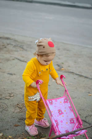Photo of a toddler girl in the funny hat playing with a toy strollerの写真素材
