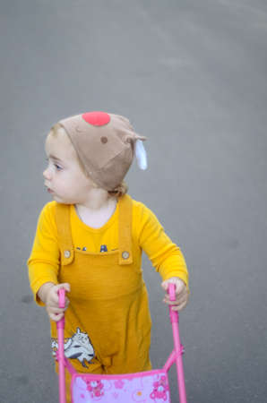 Photo of a toddler girl in the funny hat playing with a toy strollerの写真素材