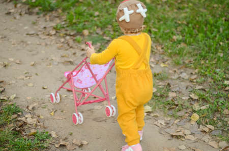 Photo of a toddler girl in the funny hat playing with a toy strollerの写真素材