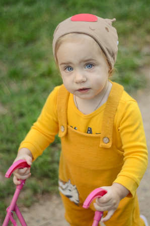Photo of a toddler girl in the funny hat playing with a toy strollerの写真素材