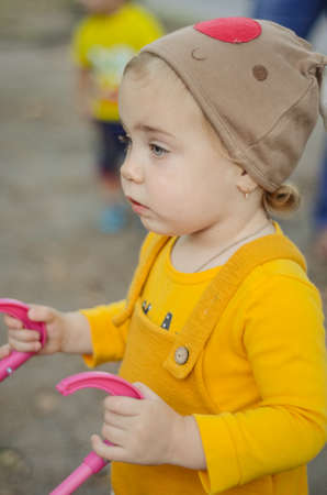 Photo of a toddler girl in the funny hat playing with a toy strollerの写真素材