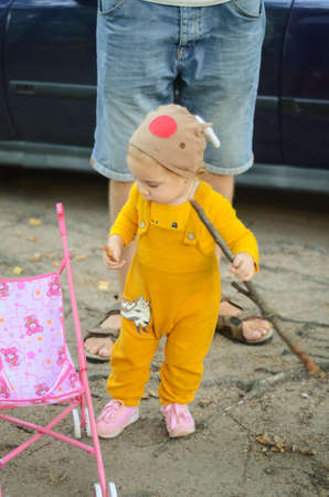 Photo of a toddler girl in the funny hat playing with a toy strollerの写真素材