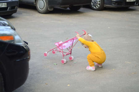 Photo of a toddler girl in the funny hat playing with a toy strollerの写真素材