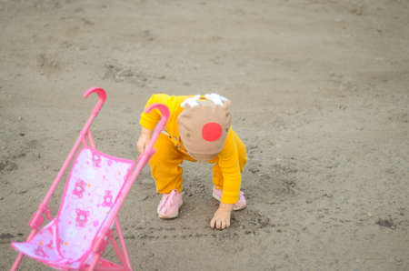 Photo of a toddler girl in the funny hat playing with a toy strollerの写真素材