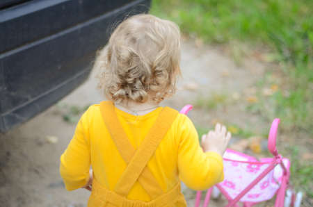 Photo of a toddler girl in the funny hat playing with a toy strollerの写真素材