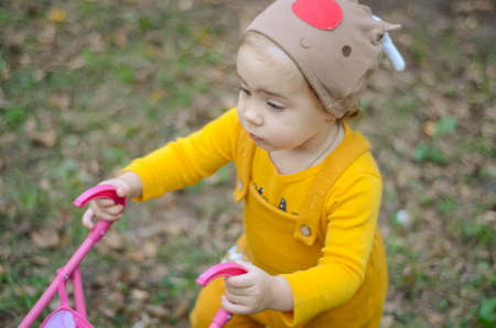 Photo of a toddler girl in the funny hat playing with a toy strollerの写真素材