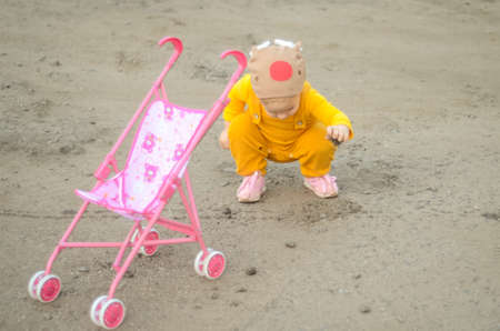 Photo of a toddler girl in the funny hat playing with a toy strollerの写真素材