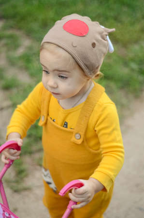 Photo of a toddler girl in the funny hat playing with a toy strollerの写真素材