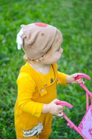 Photo of a toddler girl in the funny hat playing with a toy strollerの写真素材