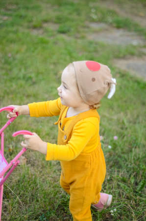 Photo of a toddler girl in the funny hat playing with a toy strollerの写真素材