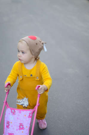 Photo of a toddler girl in the funny hat playing with a toy strollerの写真素材