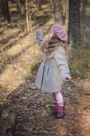 Picture of a vintage styled little girl in a beret and coat walking in the forestの写真素材