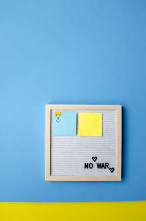 Flatlay vertical composition with a blue background, a letter board in a wooden frame with the phrase NO WAR and blue yellow stickersの写真素材