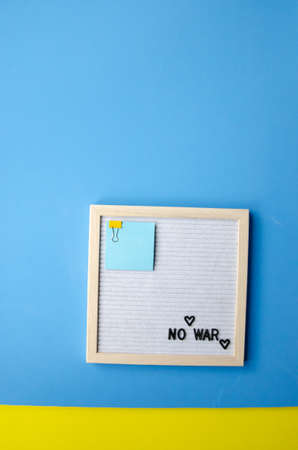 Flatlay vertical composition with a blue and yellow background, a letter board in a wooden frame with the phrase NO WAR and blue yellow stickersの写真素材