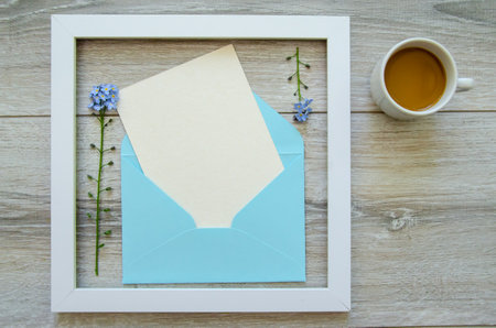 Flatlay gray natural wooden background with square white wooden frame and blue envelope white postcard copyspace, small blue flowers on a branchの写真素材