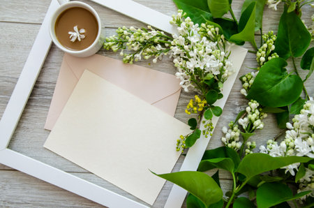 Close-up flatlay with a cup of coffee in white wooden frame and mockup and copyspace pastel pink envelopes and blank postcard framed by branches of burgundy and green leaves, whiteの写真素材