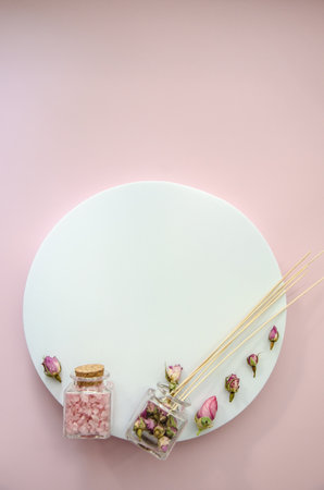 vertical Flat Lay SPA witn copy space and pink sea salt in a glass jar with a cork lid, dry pink rose buds and aromatic perfume sticks, white round mockup space for logo textの写真素材