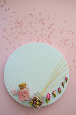 vertical Flat Lay SPA witn copy space and pink sea salt in a glass jar with a cork lid, dry pink rose buds and aromatic perfume sticks, white round mockup space for textの写真素材