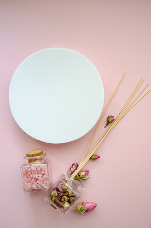 vertical Flat Lay SPA witn a lot of copy space and pink sea salt in a glass jar with a cork lid, dry pink rose buds and aromatic perfume sticks with white round mockup on top spaceの写真素材