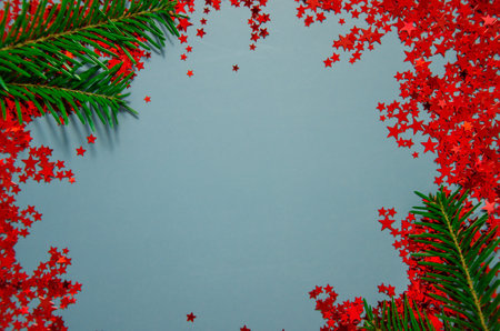 Christmas frame border. Fir tree branches decorated with red confetti stars on blue background. Christmas, winter holiday, New Year celebration concept. Greeting card mockup.の写真素材