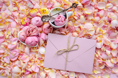 Background of pink rose buds and petals with envelope in the center and a cup of tea with rose bud and tea spoon. Flat lay, overhead view. Mother's Day, St. Valentine's Day, March 8 concept.の写真素材