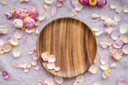 Pink and yellow rose petals and rosebuds and wooden plate on knitted pink background. Natural beauty spa concept.の写真素材