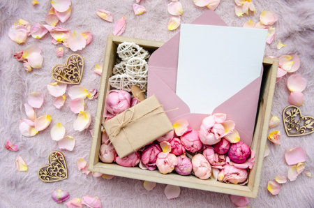 Valentine's Day Composition. Gift box with handmade gift box, craft blank card, envelope, rose buds and decorative hearts on pink background with rose petals.Copy space. Template postcard for holidayの写真素材