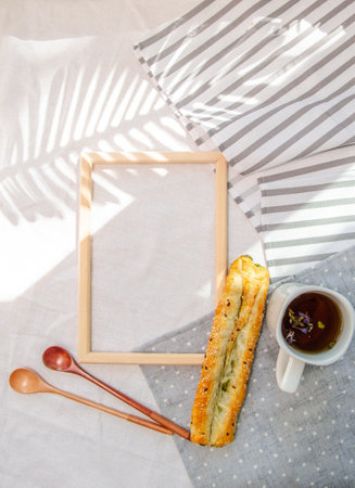 Empty frame and tasty breakfast with bakery and herbal tea and decorative wooden spoons on cotton...