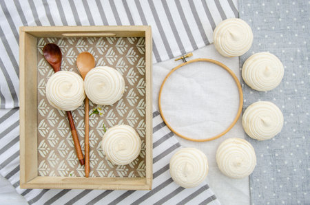 Meringue homemade zephyr marshmallows in a wooden tray with wooden spoons and round embroidery hoop frame on cotton tablecloth. mockup card. Template for recipes book or food menuの写真素材