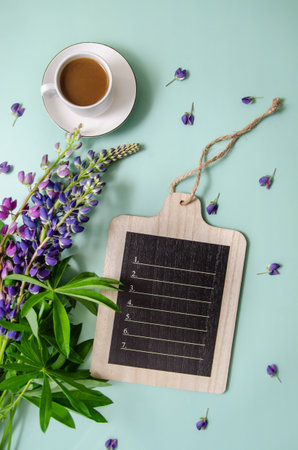 White cup of tea with lupine flowers and petals with wooden black chalk board for text on blue background. Space for text or design.の写真素材