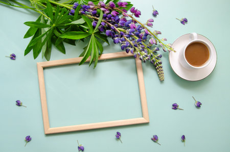 White cup of tea with lupine flowers and petals with empty wooden frame on blue background. Space for text or design.の写真素材