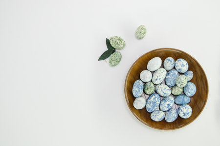 Chocolate easter eggs on a wooden plate and leaves on white background. Copy space. Easter concept, minimal design.の写真素材