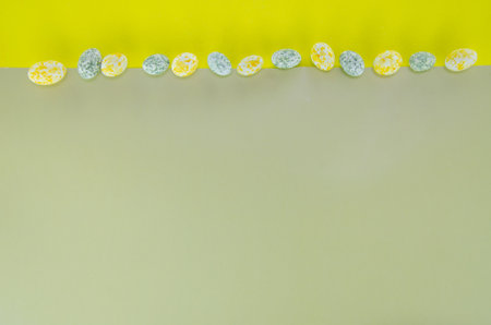 Little candy eggs on a olive-yellow background. Horizontal top-view layout for Easterの写真素材