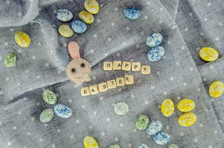 Easter concept. Easter egg shaped candies, cotton rabbit, Happy Easter letters on a cotton dotted...
