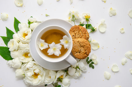A cup of herbal tea, white saucer, oatmeal cookies, composition of white roses and jasmine flowers. Mother's day card, valentine's day.の写真素材