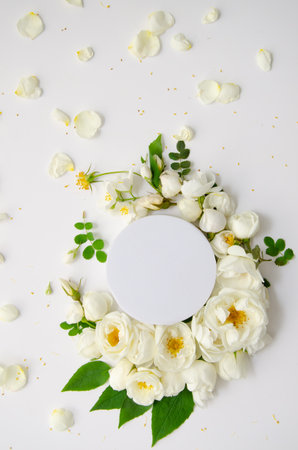 White blank round podium rounded with wreath pattern with fresh roses, rose buds, branches and leaves isolated on white background. flat lay, top view.の写真素材