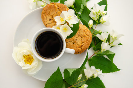 A cup of coffee, white saucer, oatmeal cookies, white roses and jasmine flowers. Mother's day card, valentine's day.の写真素材