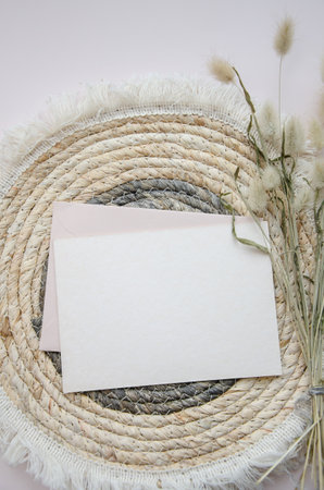 A round woven placemat, blank card and dry fluffy spikelets on a light beige background. Mock up. Concept of home comfort and interior elements. Restaurant promo. Buisness card.の写真素材