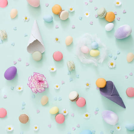 Easter creative chaos with eggs, ice cream cone macarons and flowers on the pastel green background. Flat lay composition.の写真素材