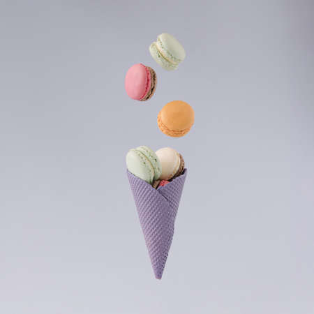 Pastel purple cone with flying sweet macarons  against gray background. minimal concept.の写真素材