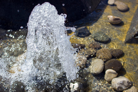 A fountain of water gushing upwards and stones in the water.