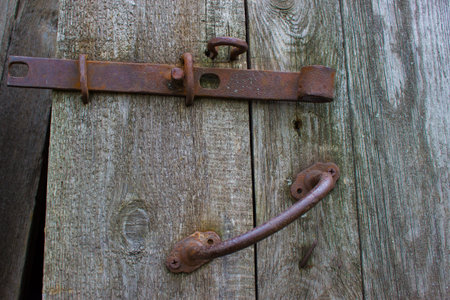 A rusty old steel bolt and handle on a wooden door.の写真素材