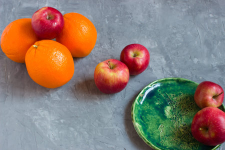 Oranges and apples on a grey concrete background and on a green ceramic handmade plate