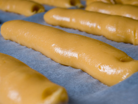 Raw dough for the eclairs lying on baking paper on a baking sheet