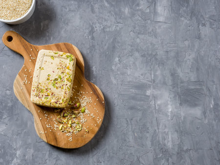 Sesame halva with pistachios on a teak chopping board on a grey background. Top view. Copy space.