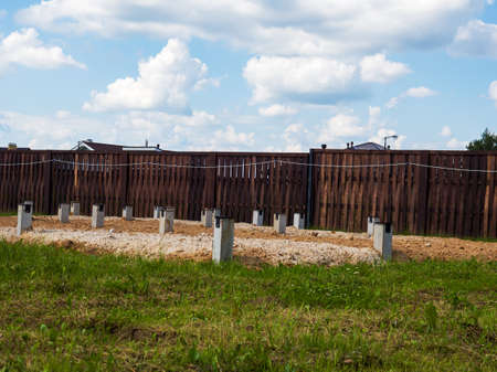 The process of building a private house. Columnar foundation on the background of a wooden fence.の写真素材