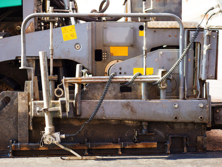 Close-up side view of a part of an road paver in the process of paving asphalt.