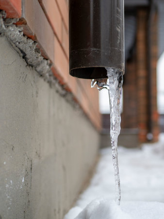 Icicle sticking out of the drainpipe. After a heavy snowstorm, the city is covered with snow and...