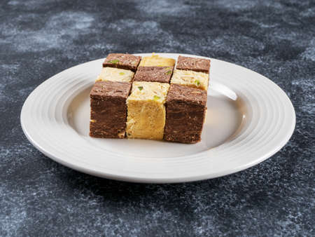 Indian sweets lying on a white plate on a black background. Assorted Indian sweets: Coconut Soan Papdi, Chocolate Soan Papdi, Premium Soan Papdi, Mango Soan Papdi. side view.の写真素材