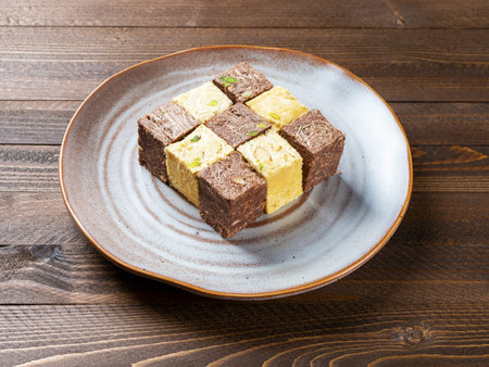 Indian sweets lying on a brown plate on a brown wooden background. Assorted Indian sweets: Coconut...